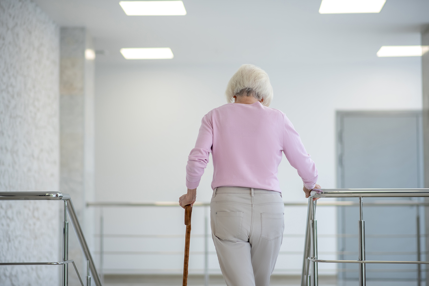 Grey-haired woman with a walking stick going upstairs